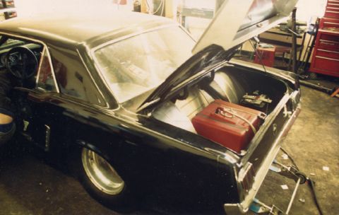 1981 Ford Bronco - Trunk of a black coupe open to reveal a red fuel cell and battery, suggesting modifications for racing.