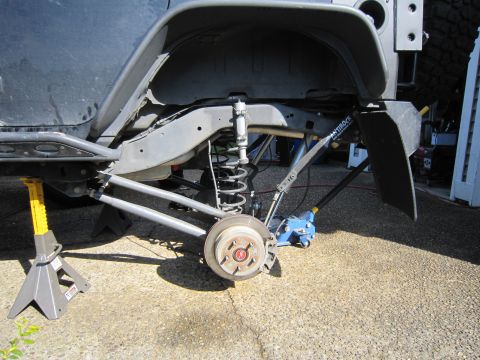 2008 Jeep Wrangler - Rear suspension exposed with the wheel removed on a Jeep sitting on a floor jack and jack stands in a driveway, showing the bare brake roto…