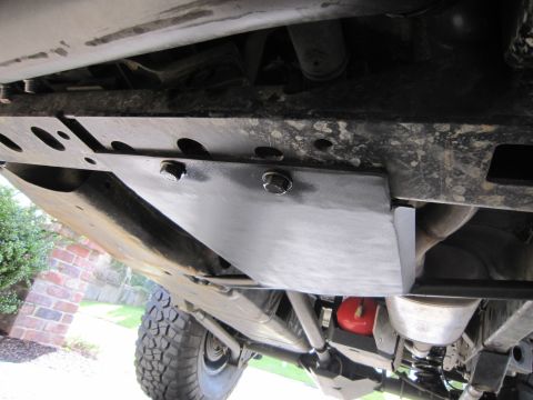 2008 Jeep Wrangler - Underbody shot looking up at a black bolt-on skid plate mounted to the boxed frame rail of a lifted Jeep, with the exhaust pipe and muffler…