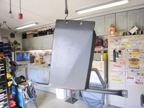 2008 Jeep Wrangler - A freshly painted black steel skid plate hanging from a ceiling hook to dry in a home garage, with its mounting crossbar and bolt holes vis…