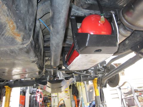 2008 Jeep Wrangler - Underside view of a raised vehicle showing a red air tank strapped into a black fabricated cradle bolted to the frame, with a brass fitting…