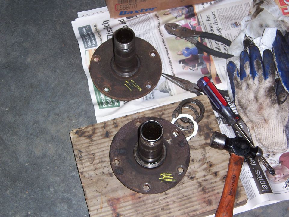 Two rusty wheel hubs with tools and gloves on newspaper