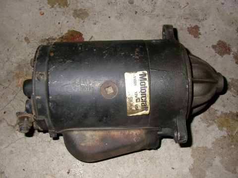 1990 Ford Bronco - dirty black Motorcraft 12-volt starter motor with a faded label, lying on a paint-spattered surface.