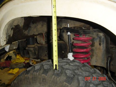 1989 Ford Bronco - A tape measure is used to measure the suspension components of a vehicle's wheel well.