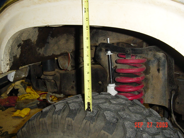Measuring tape at red coil spring suspension over off-road tire in wheel well