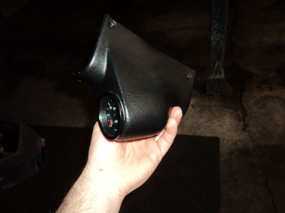 Black textured gauge pod held in hand, with a black gauge showing red needle