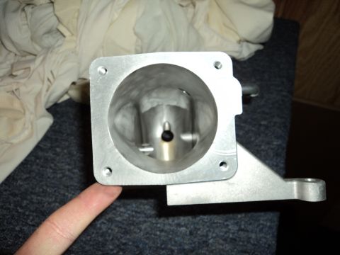 2004 Mercury Grand Marquis - A close-up view of a metal throttle body part, held by a finger, with a mounting bracket attached.