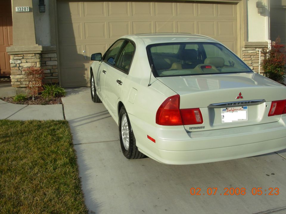 White sedan parked in driveway, rear 3/4 view. Visible badge on trunk