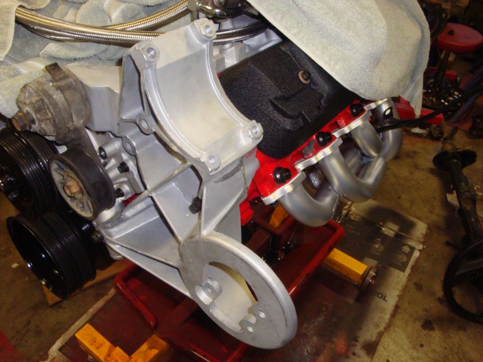 Engine block with silver exhaust manifold and red valve cover, mounted on a red stand