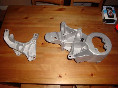 1989 Ford Bronco - Two engine mounting brackets are displayed on a wooden surface, with a box and a red object in the background.