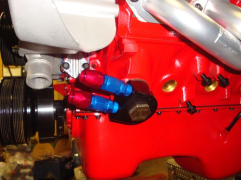 1989 Ford Bronco - Close-up view of an engine block an oil filter housing with attached red and blue oil cooler lines.