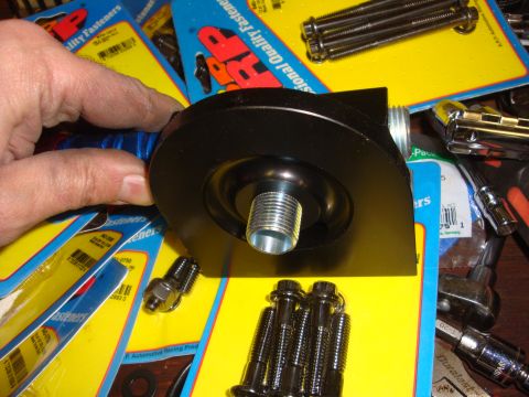 1989 Ford Bronco - A black oil filter adapter is held by a hand, with various fasteners and packaging visible in the background.