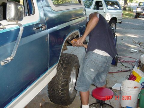 1989 Ford Bronco - A person uses an angle grinder on the rear fender of a blue and white 1989 Ford Bronco, with another Bronco visible in the background.
