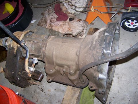 1992 Jeep YJ - A transmission assembly is shown on a garage floor, with various automotive parts and tools scattered around.