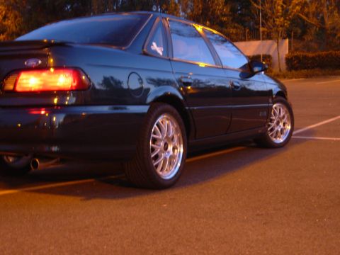 1995 Ford Taurus - The rear quarter of a 1995 Ford Taurus is shown, aftermarket wheels and a dark paint color.
