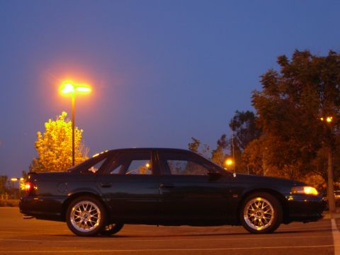 1995 Ford Taurus - Side view of a 1995 Ford Taurus parked under streetlights during twilight.