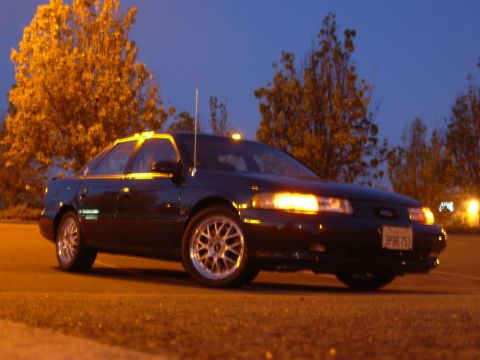 1995 Ford Taurus - A 1995 Ford Taurus sedan is parked at night, its headlights and side markers illuminated.
