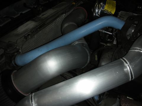 1998 Ford Crown Victoria - dim engine bay view of polished aluminum charge pipes and a blue silicone hose routed near the radiator.