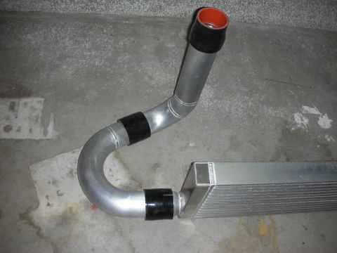 1998 Ford Crown Victoria - mandrel-bent aluminum charge pipe joined by black couplers to an intercooler end, with an orange silicone elbow, on concrete.