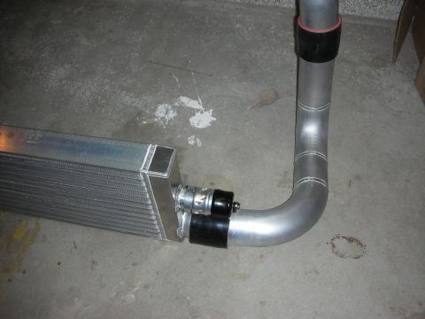 1998 Ford Crown Victoria - aluminum charge pipe connected to an intercooler end tank with a fitting, photographed on a concrete garage floor.