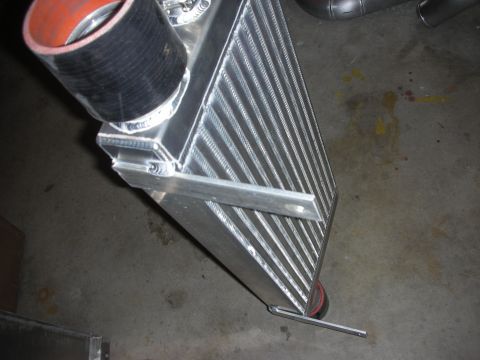 1998 Ford Crown Victoria - aluminum intercooler with a welded diagonal support bar and a black silicone coupler, resting on a shop floor.
