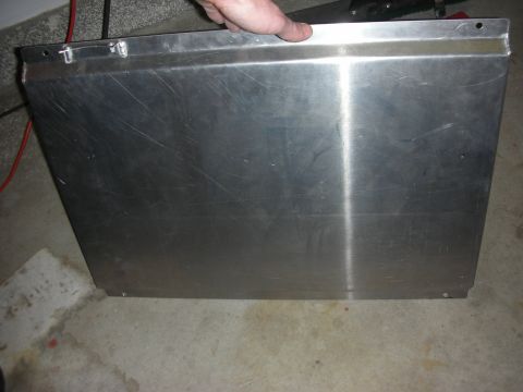 1998 Ford Crown Victoria - hand steadies a large scratched brushed-aluminum panel with bolt holes along its edges, set on a shop floor.