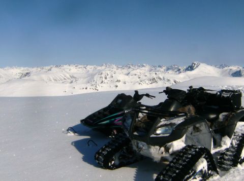 2000 Ford E350 - Snowmobiles and an ATV are parked in a snowy mountain landscape under a clear blue sky.