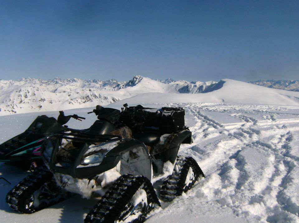 ATV with tracks in snowy mountains, another snowmobile visible