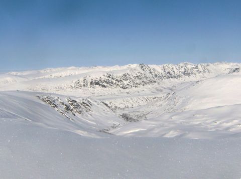 2000 Ford E350 - A vast, snow-covered valley stretches between , mountainous terrain under a bright blue sky.