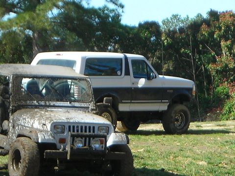 1995 Ford Bronco - A white and dark blue Ford Bronco is visible behind a mud-covered Jeep Wrangler in an outdoor setting.