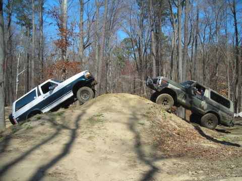 1995 Ford Bronco - Two Ford Broncos navigate a challenging dirt trail in a wooded area.