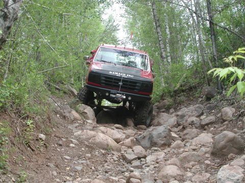 1986 Jeep J-10 - A red truck with a black hood and winch navigates a challenging rocky trail.