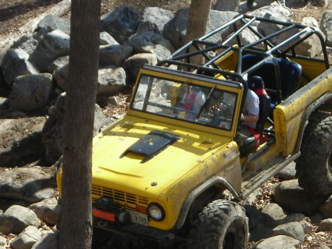 1995 Ford Bronco - Yellow Bronco modified for off-roading navigates a rocky trail.
