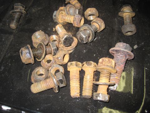 1979 Ford Bronco - A collection of various rusty bolts and nuts are scattered across a dark surface.