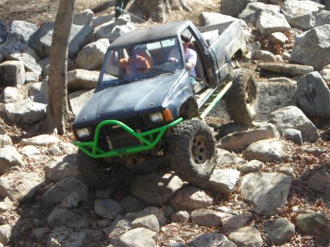 1995 Ford Bronco - This modified pickup truck is navigating a rocky trail with two occupants.