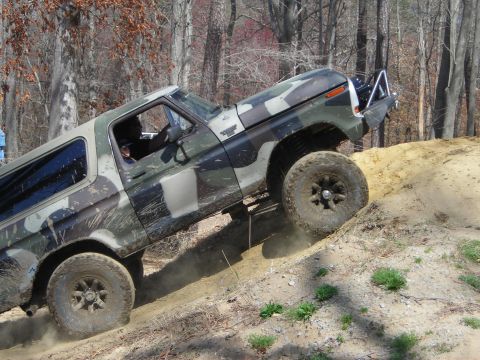 1995 Ford Bronco - This Ford Bronco, painted in camouflage, navigates an off-road trail by climbing a steep dirt incline.