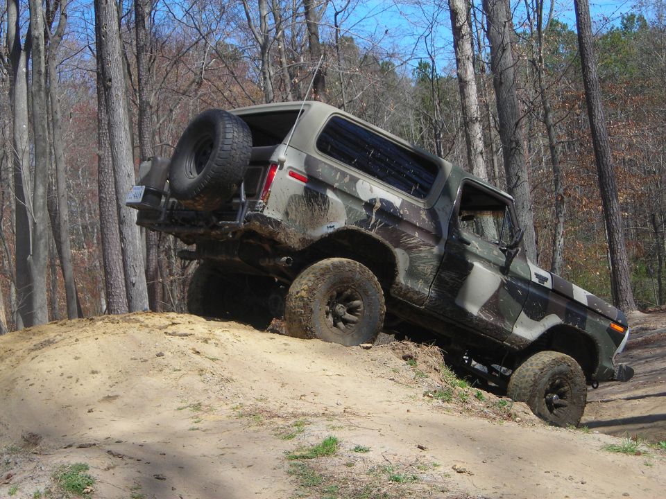 Camouflaged Ford Bronco climbing a dirt hill off-road