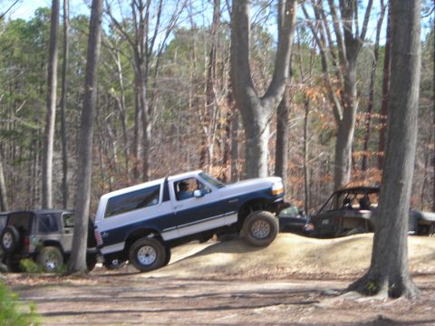 1995 Ford Bronco - Two off-road vehicles, a Ford Bronco and a Jeep Wrangler, navigate a wooded trail.