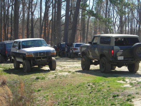 1995 Ford Bronco - Several off-road vehicles are gathered in a clearing surrounded by trees.