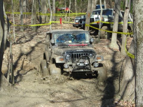 1995 Ford Bronco - A Jeep Wrangler navigates a muddy obstacle course with caution tape marking the path.