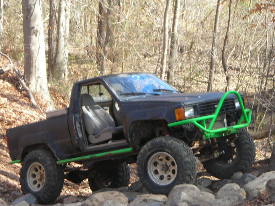 Black pickup truck with green off-road bumper and roll cage on rocky terrain