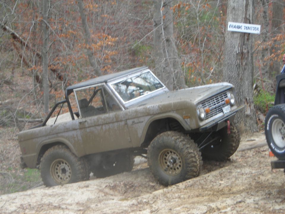 Mud-covered 1970 Ford Bronco with off-road tires on a dirt trail