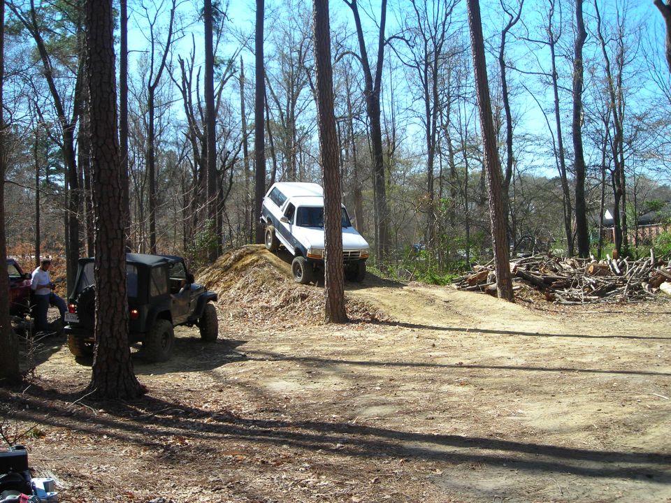 1995 Ford Bronco climbing a dirt mound, with a Jeep in the foreground