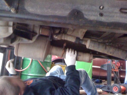1996 Ford C-350 (Centurion Conversions) - A mechanic works on the exhaust system of a vehicle, focusing on the muffler and driveshaft components.