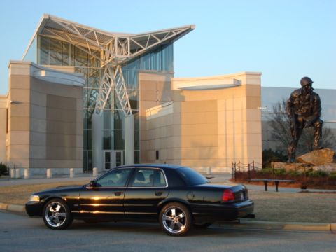 2004 Ford Crown Victoria - A black 2004 Ford Crown Victoria is parked in front of a contemporary building with a statue in the background.