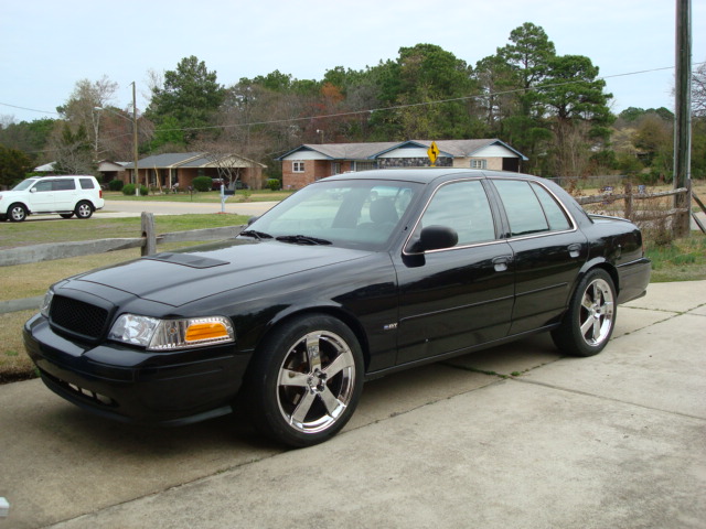 Black 2004 Ford Crown Victoria parked in driveway, white SUV in background