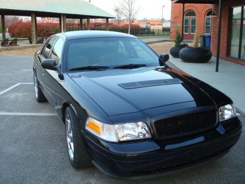 2004 Ford Crown Victoria - This black sedan, likely a Ford Crown Victoria from the early 2000s, is shown from a three-quarter front angle.