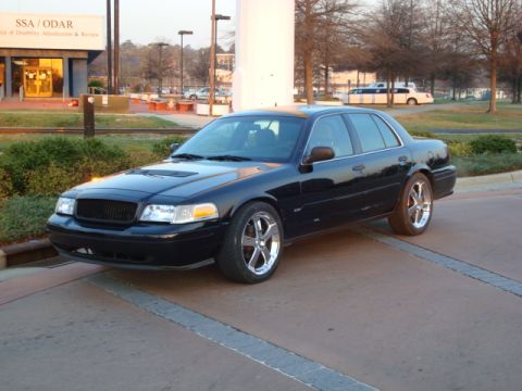 2004 Ford Crown Victoria - A black 2004 Ford Crown Victoria is parked outside a building with trees in the background.