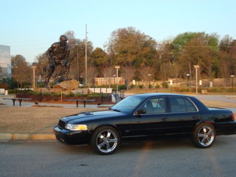2004 Ford Crown Victoria - A black 2004 Ford Crown Victoria is parked on the side of the road with a statue in the background.