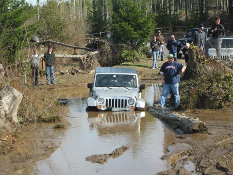 2008 Jeep Wrangler - A group of people watch as a Jeep Wrangler navigates a muddy trail with a large water hazard.